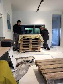 Twee mensen zetten de lege bak van twee meter op zijn plaats, op een stapel pallets